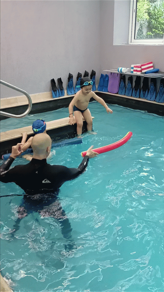 enfant saute dans l'eau avec frite avec l'aide d'un maitre nageur dans l'eau